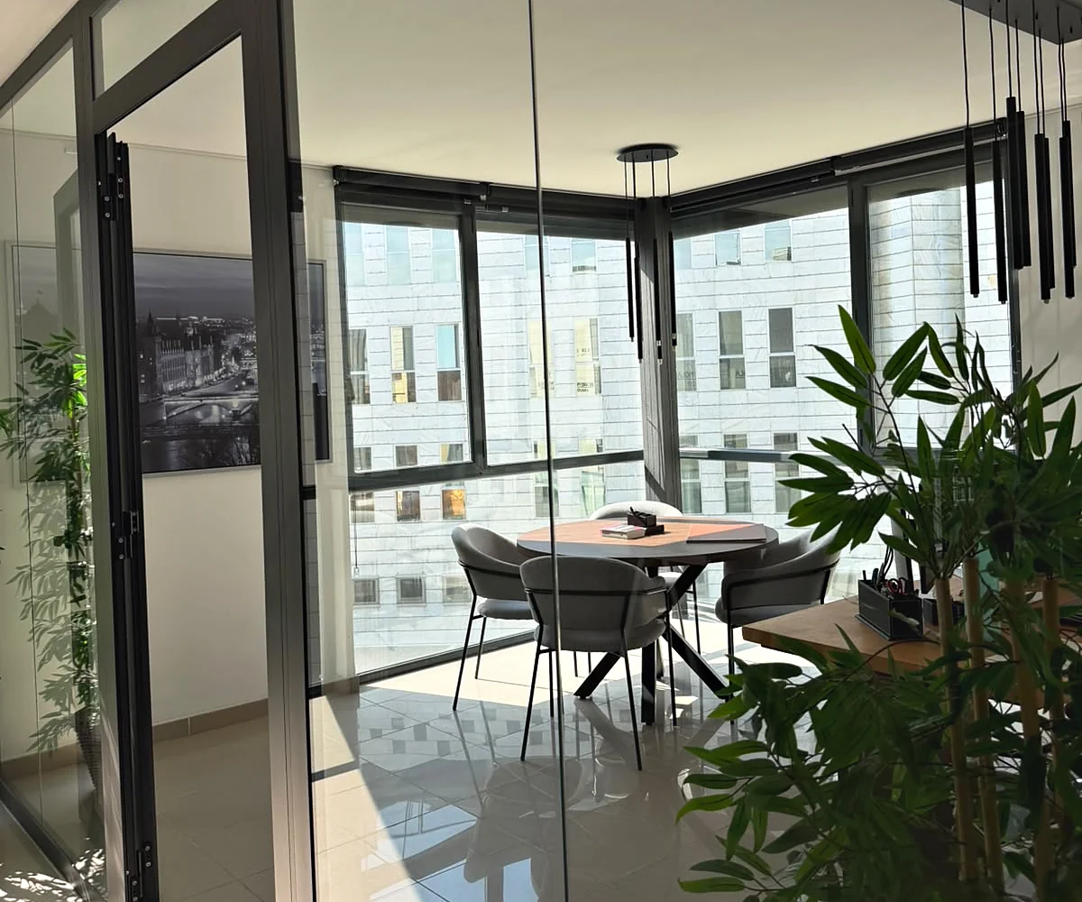 Espacio de reuniones visto a través de la zona acristalada, con mesa, sillas y luz natural.